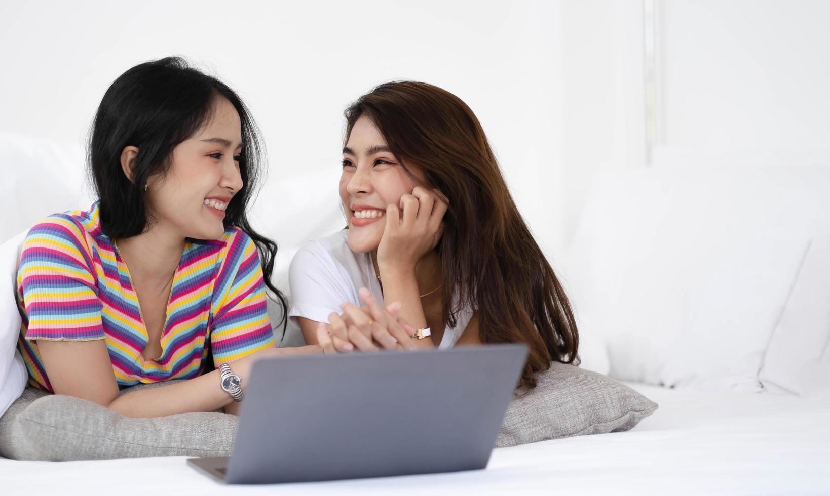 jonge Aziatische lgbt-lesbische stellen gebruiken laptops om informatie te zoeken om een nieuw huis te kopen. terwijl ze elkaar omhelzen in bed. foto