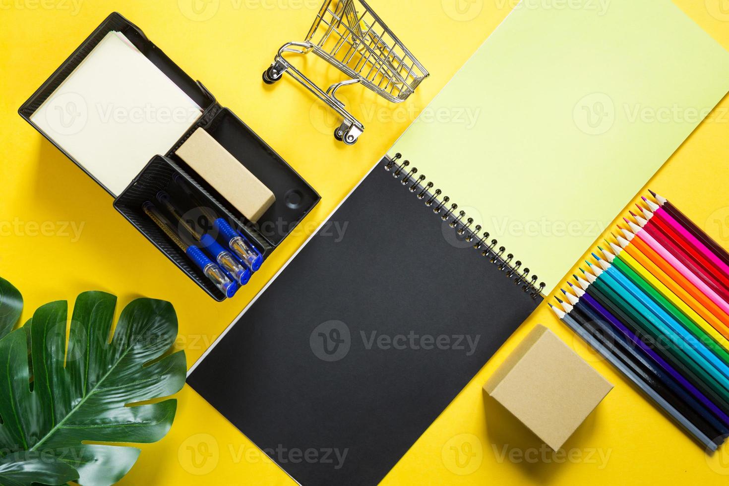 lay-out van veelkleurig briefpapier op een gele achtergrond spiraalvormig notitieboekje, kleurpotloden, standaard, pennen, binnenbloem. zakelijk plat leggen, bespotten. vellen voor notities, kantoorwerk. terug naar school foto