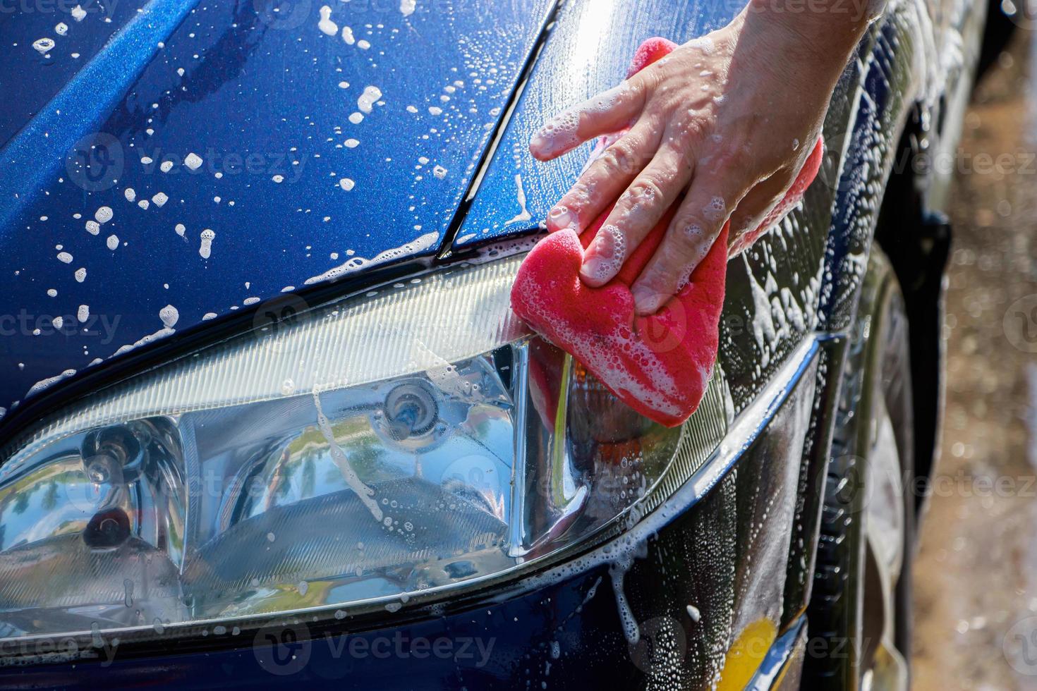 man wast auto buiten. handreinigende auto. mannelijke hand met roze spons met schuim. foto