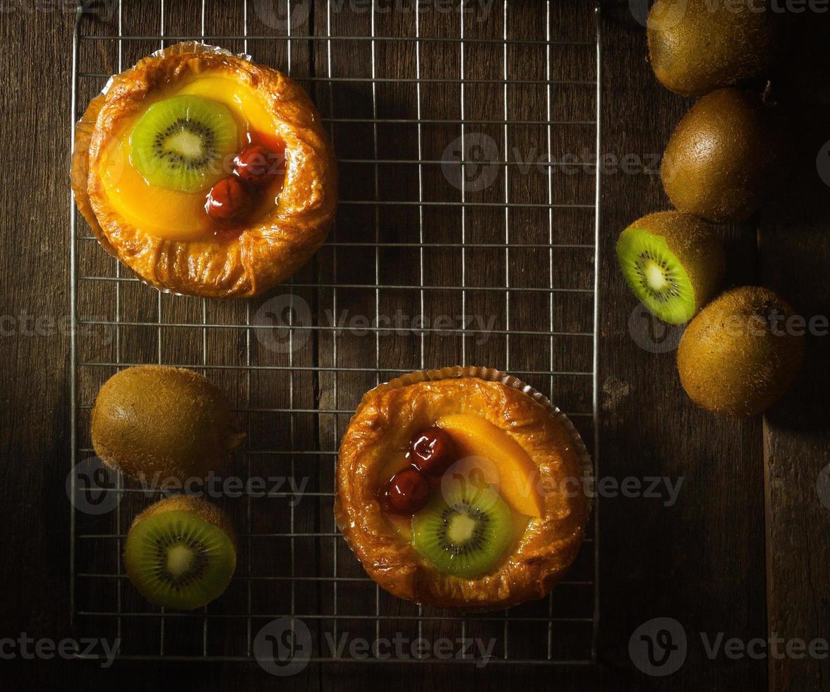 fruittaart met kiwi, kers, persimmon, op stalen strip op de houten bank gezet met een zwarte achtergrond, bovenaanzicht foto