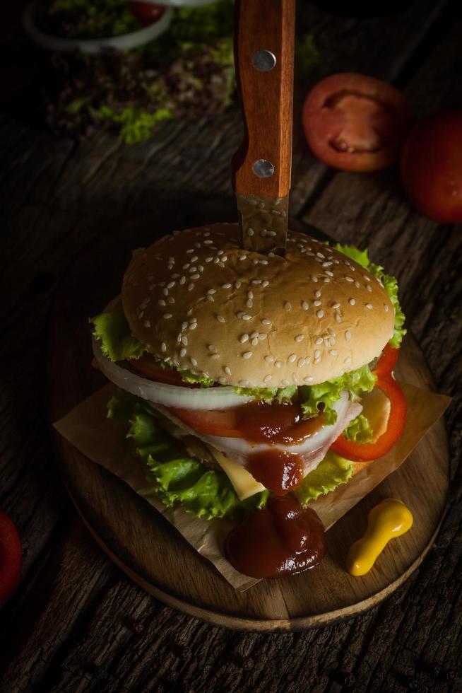 varkensvlees hamburger zelfgemaakte met gegrild spek bevat groenten, kaas, sla, ui, chili, kruiden in een houten schotel op een houten vloer. foto