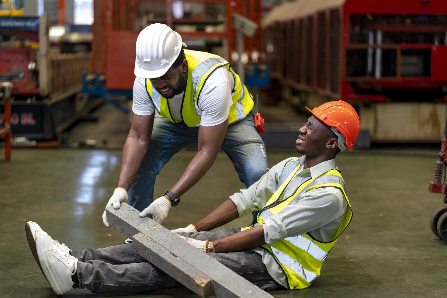 Afro-Amerikaanse fabrieksarbeider die een ongeluk krijgt tijdens het werken op de productielocatie terwijl zijn collega helpt voor een veiligheidswerkplek en noodconcept foto