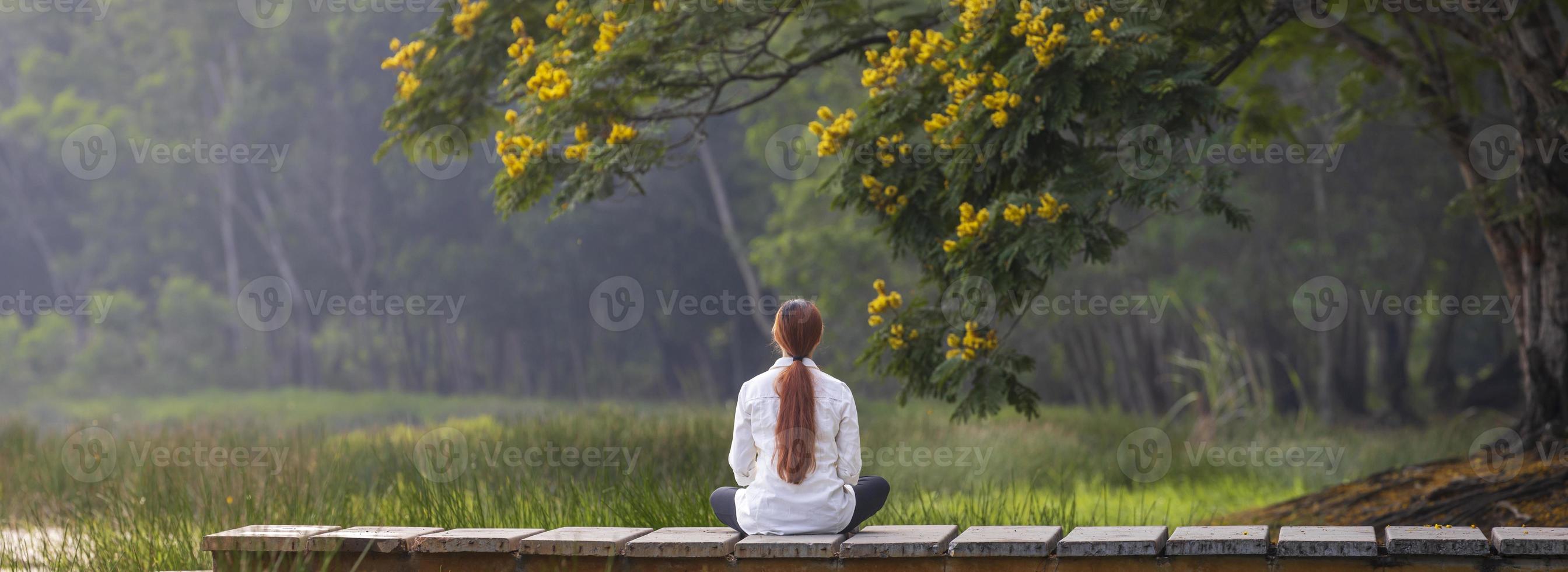 panorama achteraanzicht van een vrouw die ontspannen meditatie beoefent in het openbare park om geluk te bereiken vanuit innerlijke vrede wijsheid met gele bloembloesem in de zomer foto