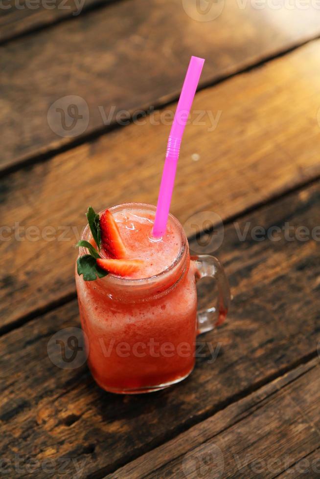 glas aardbeiensmoothie en verse aardbeien bovenop en hebben een houten ondergrond. gezond eten en drinken concept. foto