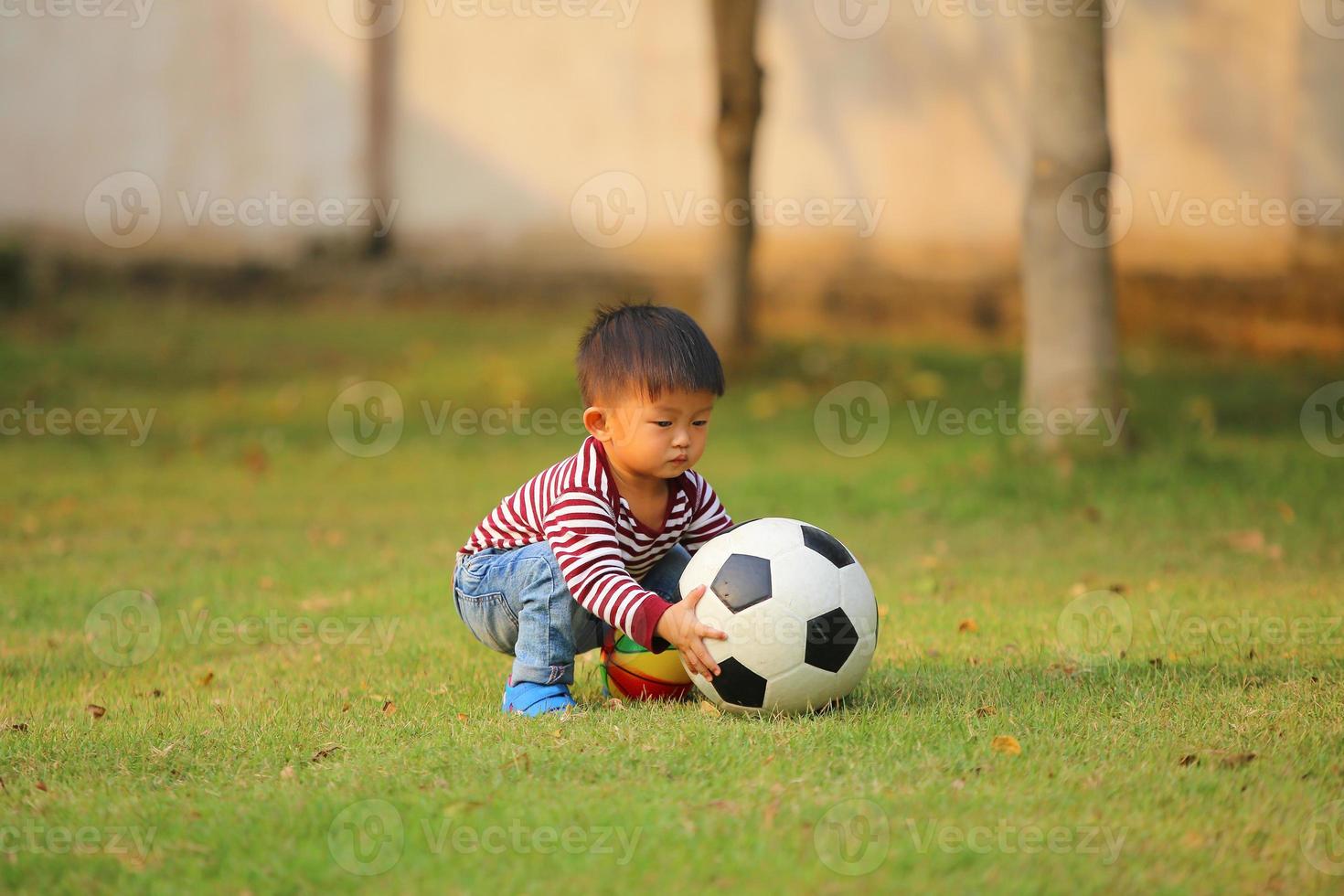 Aziatische jongen voetballen in het park. kind met bal speelgoed in grasveld. foto