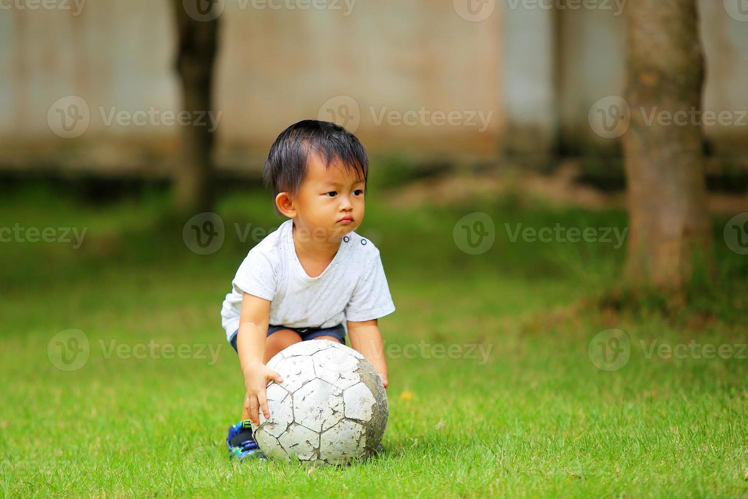 Aziatische jongen voetballen in het park. kind met bal in grasveld. foto