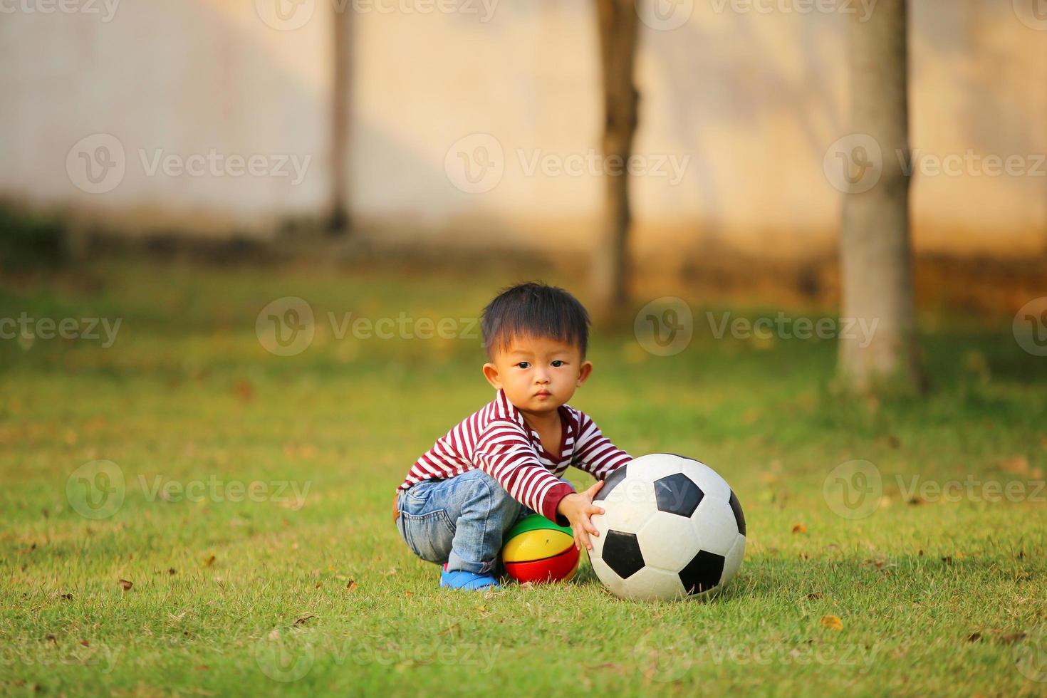 Aziatische jongen voetballen in het park. kind met bal speelgoed in grasveld. foto