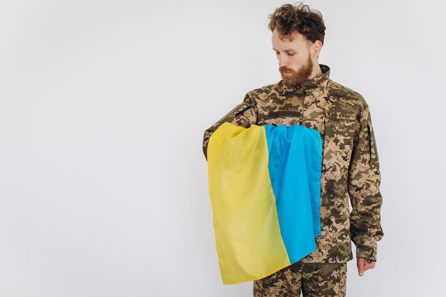 portret van een emotionele jonge, bebaarde Oekraïense patriot-soldaat in militair uniform met een vlag op kantoor foto