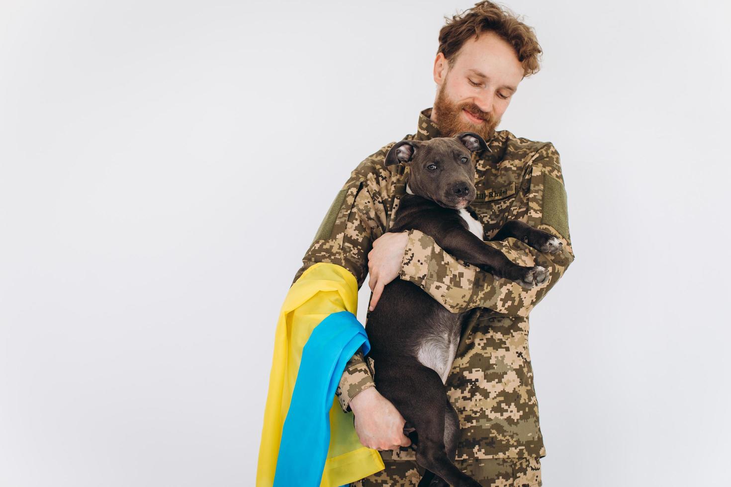 Oekraïense soldaat in militair uniform met een gele en blauwe vlag houdt een hond in zijn armen op een witte achtergrond foto