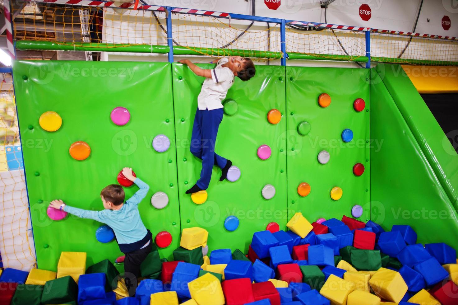 twee broers kinderen klimmen op een groene muur in attractie speeltuin. foto