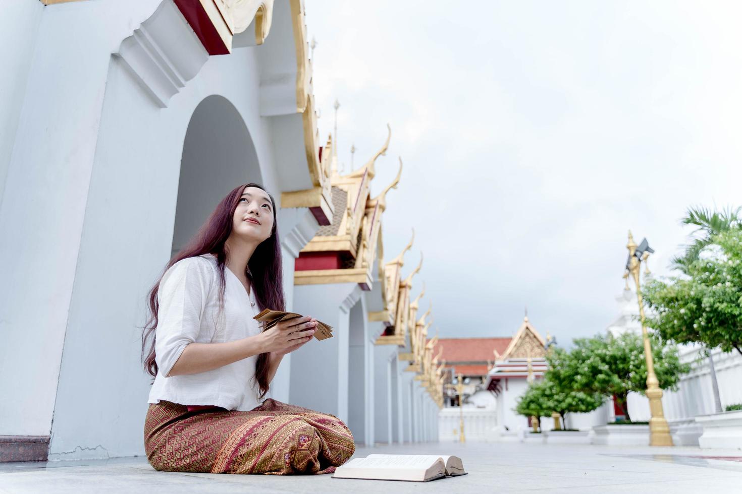 azië vrouw draagt traditionele kleding van thailand kijk boeddhabeeld en houd sanskriet oude tripitaka boek van heer boeddha dhamm foto