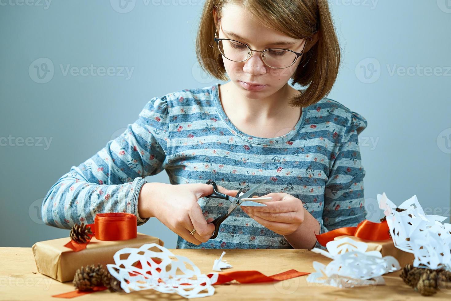 meisje tiener met bril sneeuwvlokken uit papier snijden. conceptvoorbereiding voor het nieuwe jaar. foto