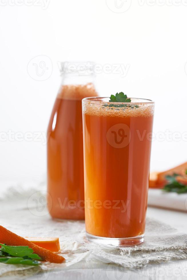 een glas vers geperst wortelsap met kruiden op de achtergrond van een fles sap. foto