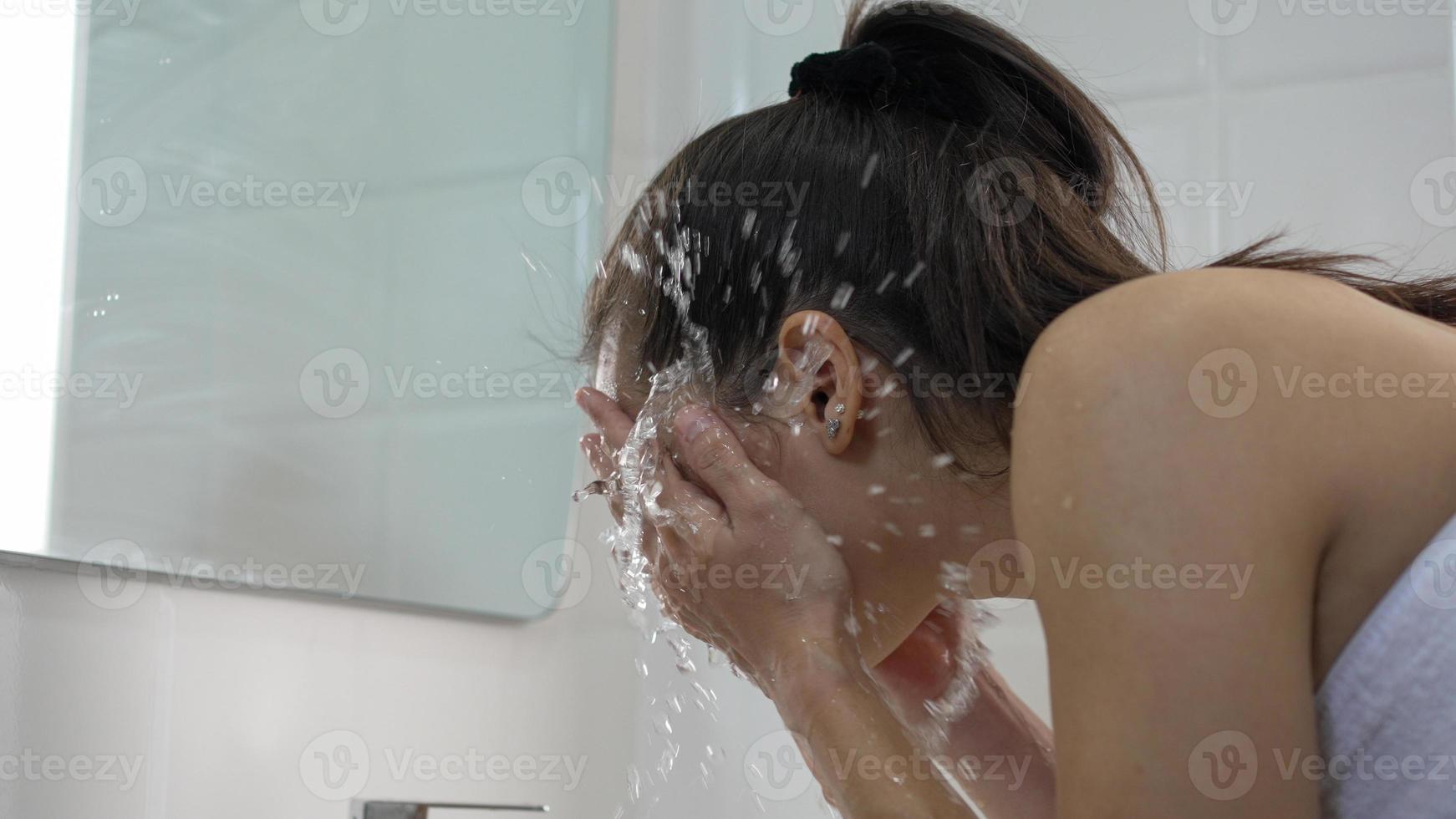 jonge vrouw die haar gezicht thuis in de badkamer wast foto