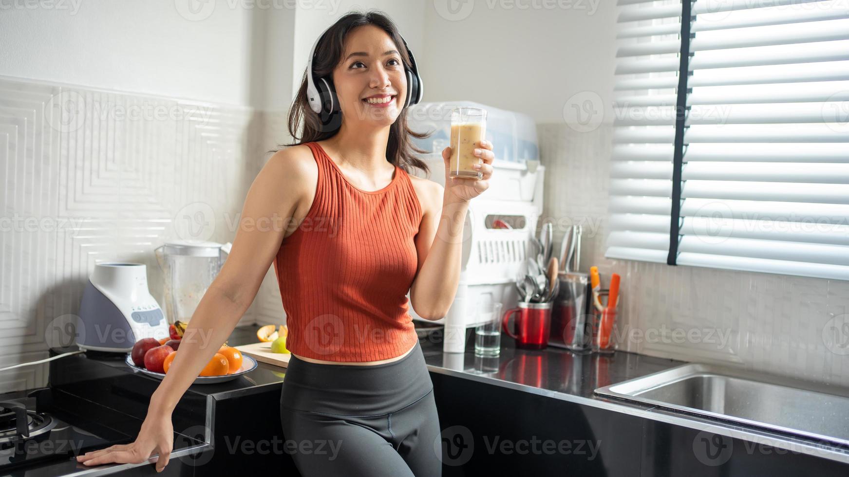 mooie jonge vrouw die smoothies maakt en drinkt van fruit in de keuken thuis terwijl ze naar muziek luistert via een koptelefoon - lifestyle concepten foto