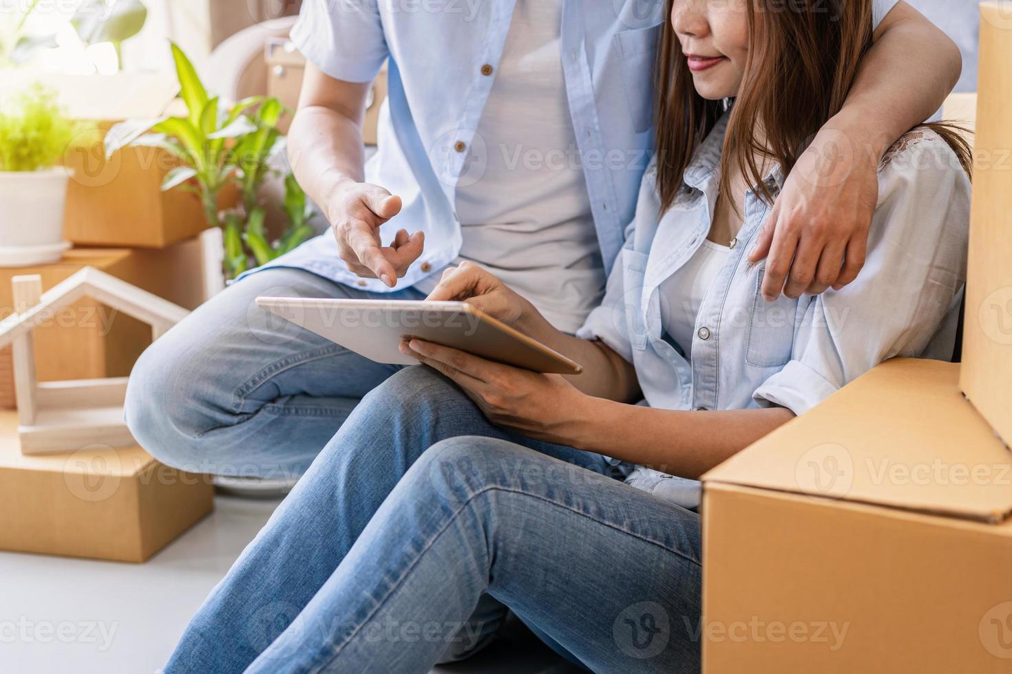 jong gelukkig stel verhuizen naar een nieuw huis, zittend en ontspannend op de vloer en op zoek naar ideeën voor huisdecoratie op tablet foto