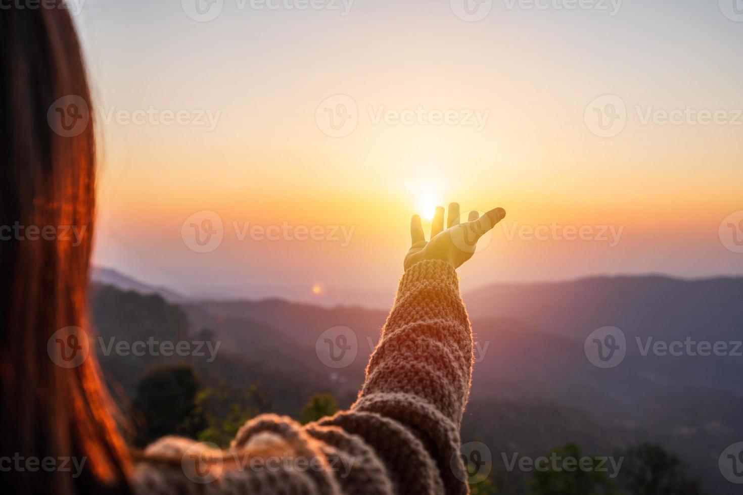 jonge vrouwenhand die naar de bergen reikt tijdens zonsondergang en een prachtig landschap foto