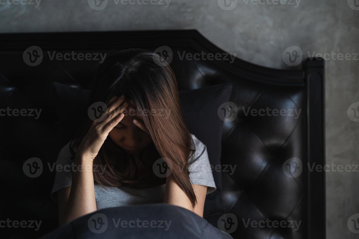 eenzame jonge vrouw depressief en gestrest zittend in de donkere slaapkamer, concept van negatieve emoties foto