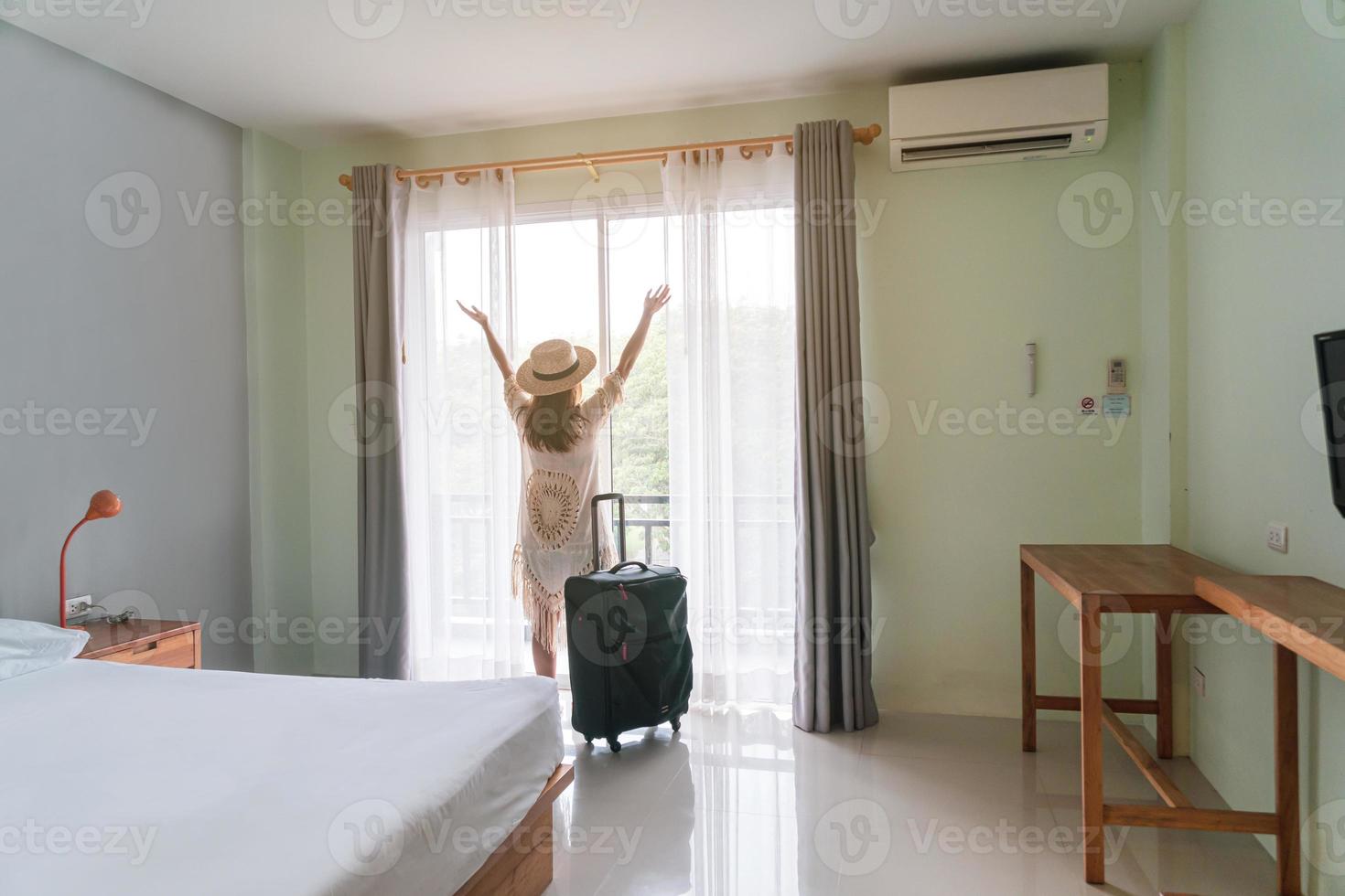 jonge vrouw reiziger met bagage kijken naar uitzicht in hotelkamer op zomervakantie foto