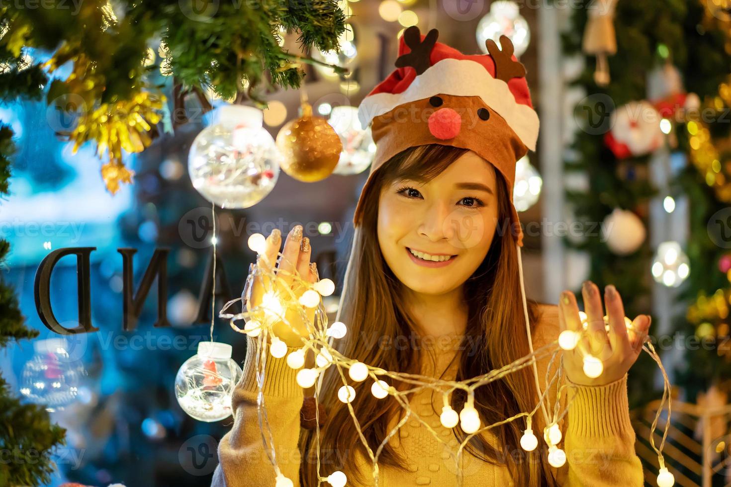 vrolijk kerstfeest, lachende mooie jonge aziatische vrouw met een gloeiende kerstslinger foto