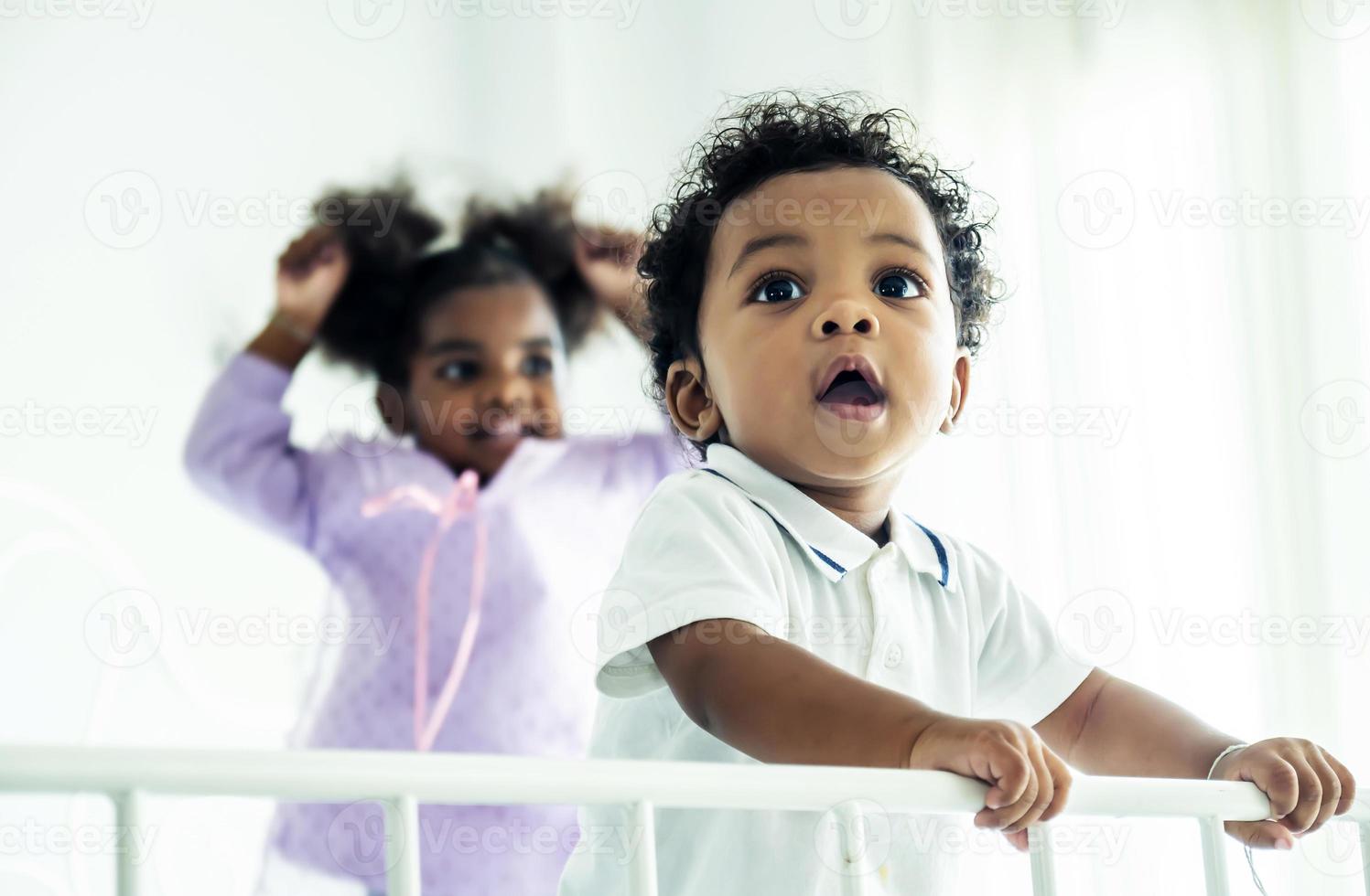 gelukkige afro-amerikaanse ondeugende kinderen jongen en meisje springen op het bed met geluk. twee grappige kleine energieke gemengd ras kinderen broer met zus plezier spelen op bed foto
