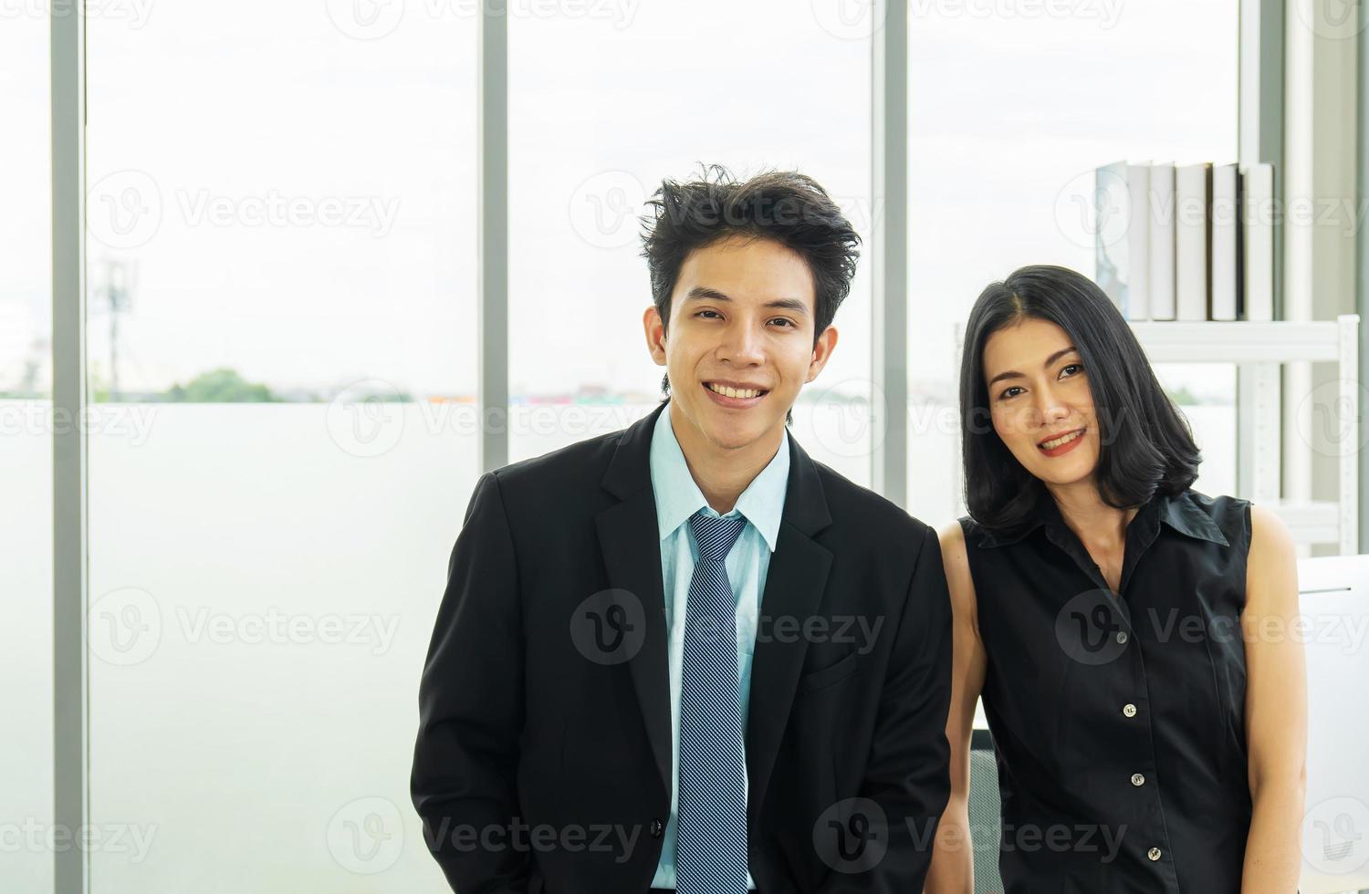 concept van partnerschap in het bedrijfsleven. een man in een pak en een vrouw in een zwarte jurk die op kantoor staan en met een zelfverzekerde glimlach naar de camera kijken naar het succes van hun partnerschap foto