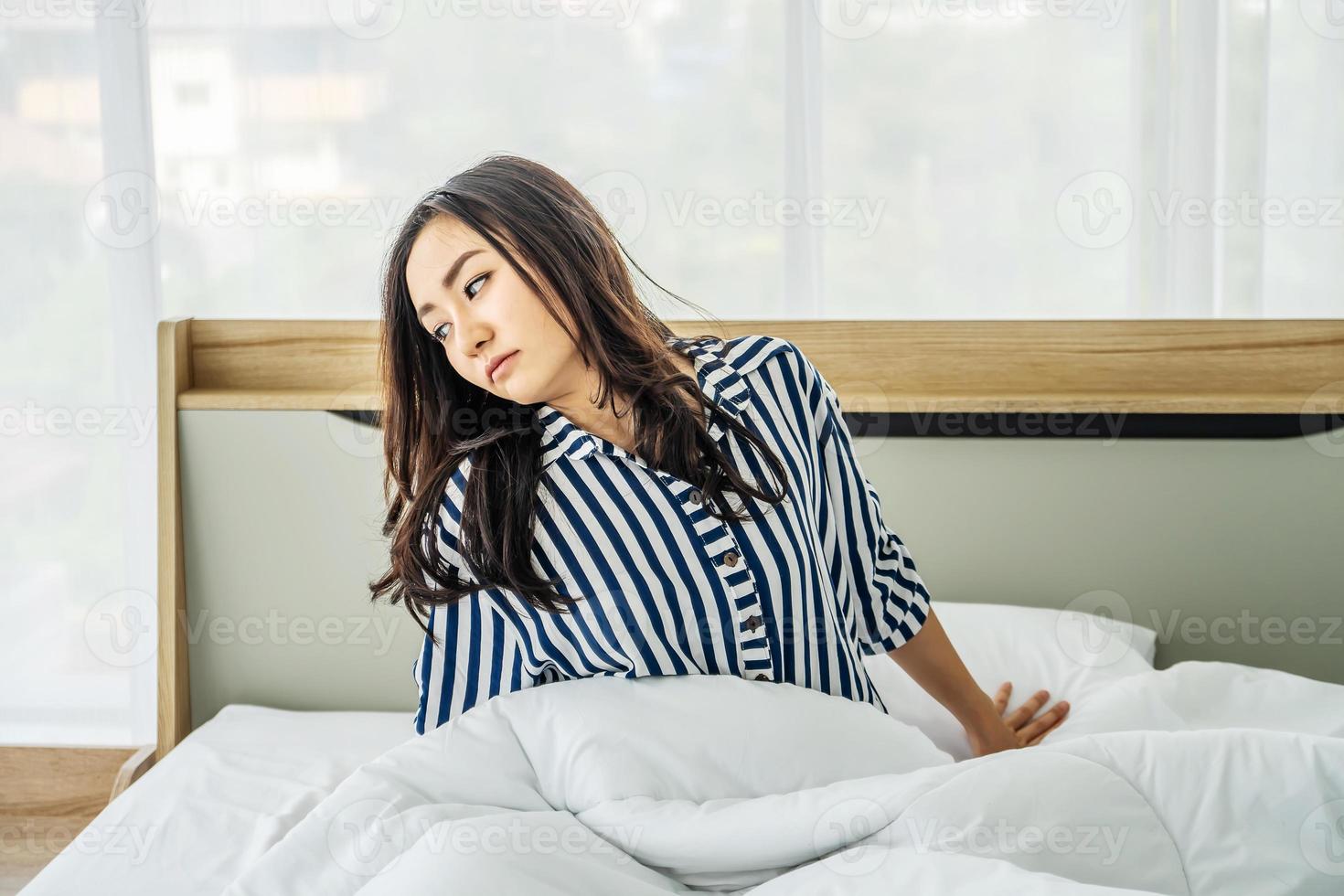 jong aziatisch meisje dat zich gelukkig uitstrekt in bed na het wakker worden in de ochtend. portret van mooie aziatische vrouw die geniet van verse, zachte beddengoedmatras in de slaapkamer. foto