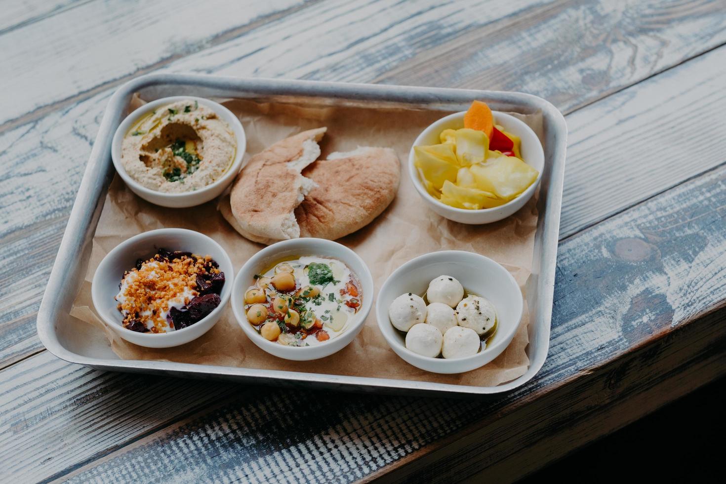 traditioneel Israëlisch voedselconcept. kom met exotische schotel op dienblad. hummus, groenten met kruiden. Pita brood. heerlijk ontbijt. geitenkaas. foto