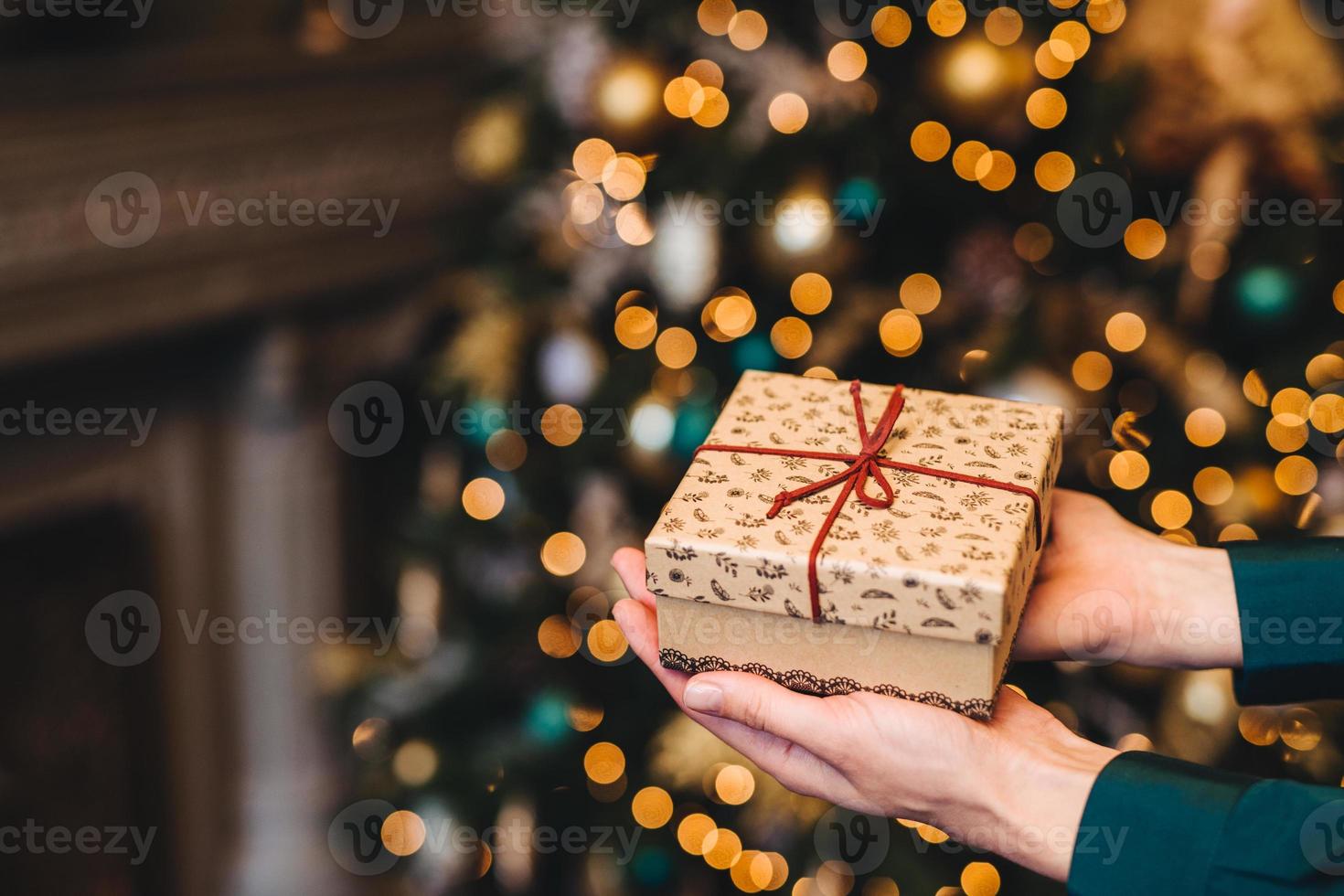 hirizontal shot van mooie verpakte huidige doos in handen van de vrouw tegen versierde kerst- of nieuwjaarsboom. nieuwe jaar achtergrond. focus op geschenkdoos. viering concept. foto