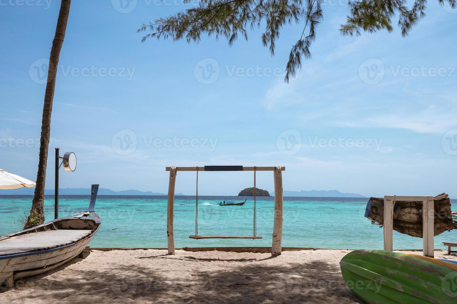 houten schommel op het strand met houten boot zeilen op tropische zee foto