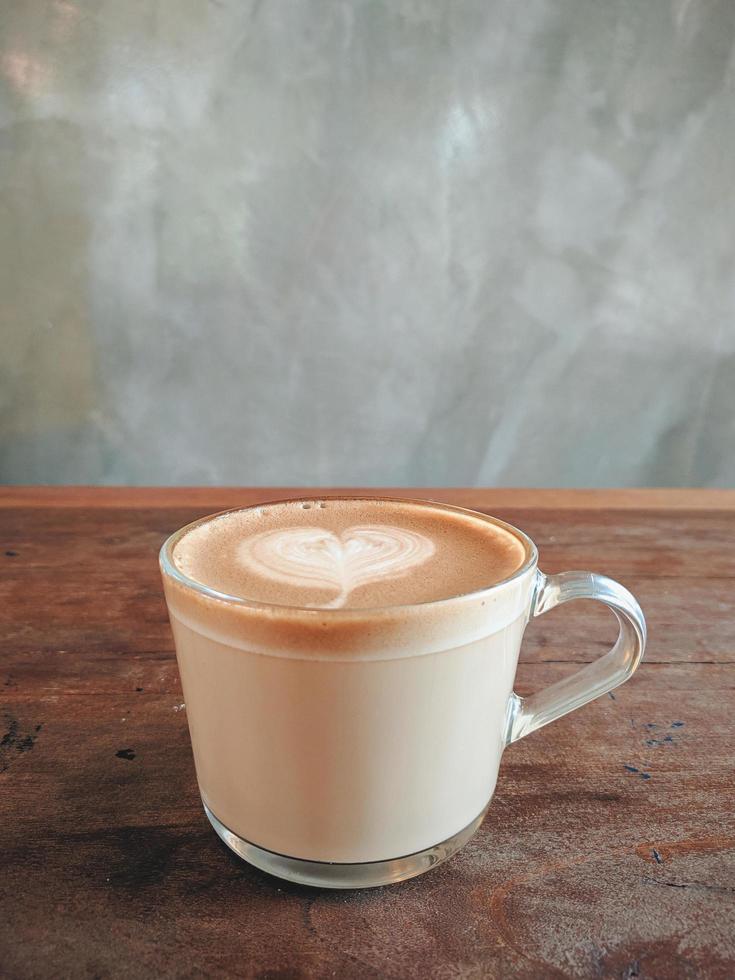 hete latte witte koffie in glas met hartvorm latte art op bruine oude houten tafel in café, eten en drinken concept. foto