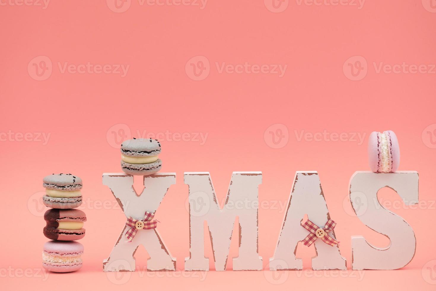 het houten woord xmas met kleurrijke bitterkoekjes of macarons op roze achtergrond foto