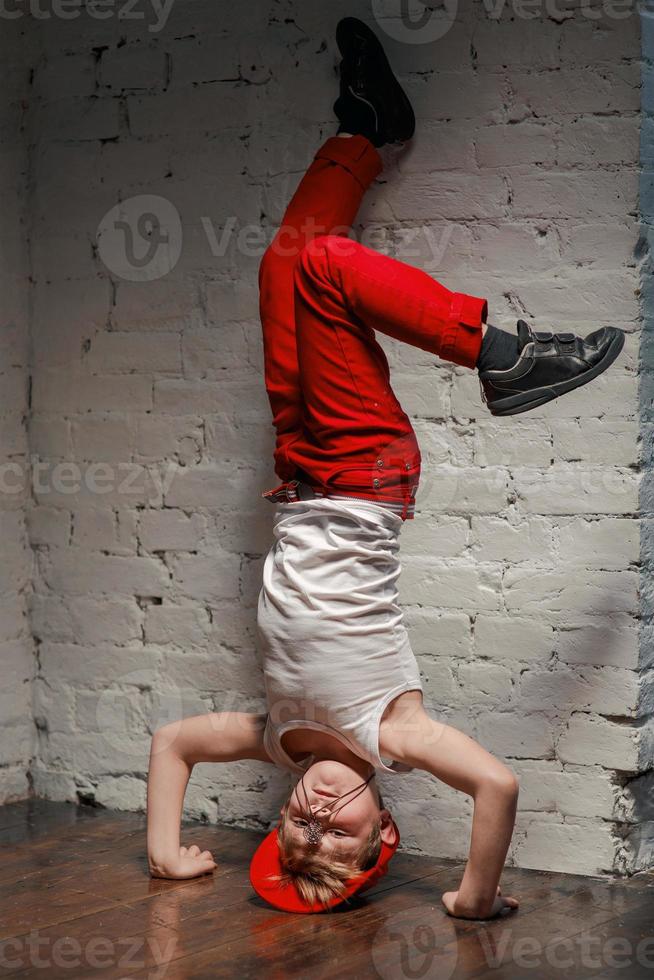 portret van een coole jonge hiphopjongen in een rode hoed en een rode broek en een wit overhemd in de loft foto