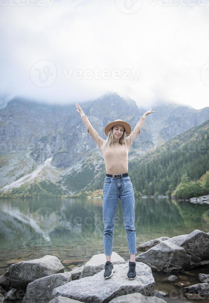 jonge toeristenvrouw in een hoed met handen omhoog op de top van de bergen foto