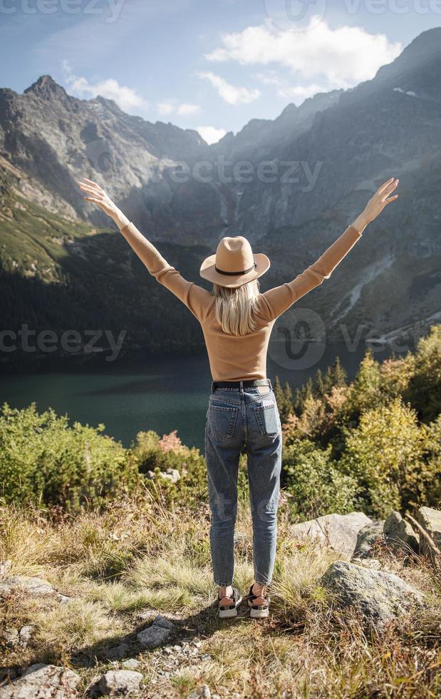 jonge toeristenvrouw in een hoed met handen omhoog op de top van de bergen foto