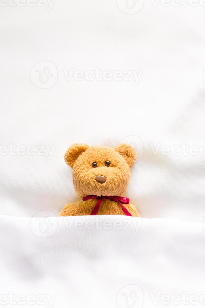 teddybeerpop liggend in het witte bed foto