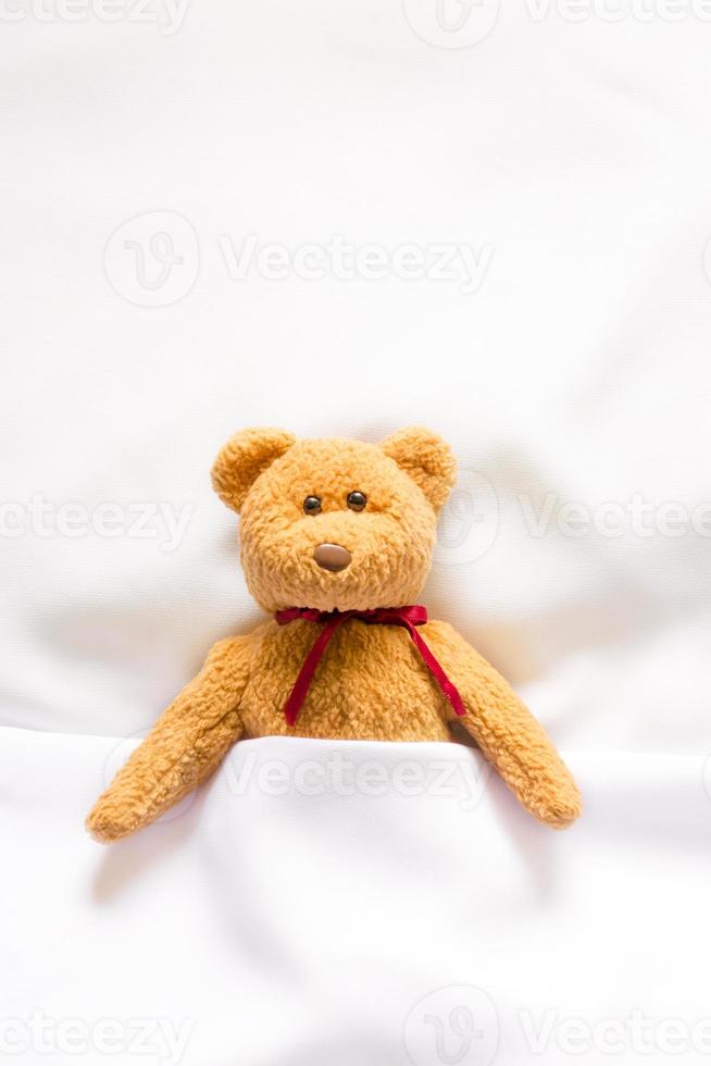 teddybeerpop liggend in het witte bed foto