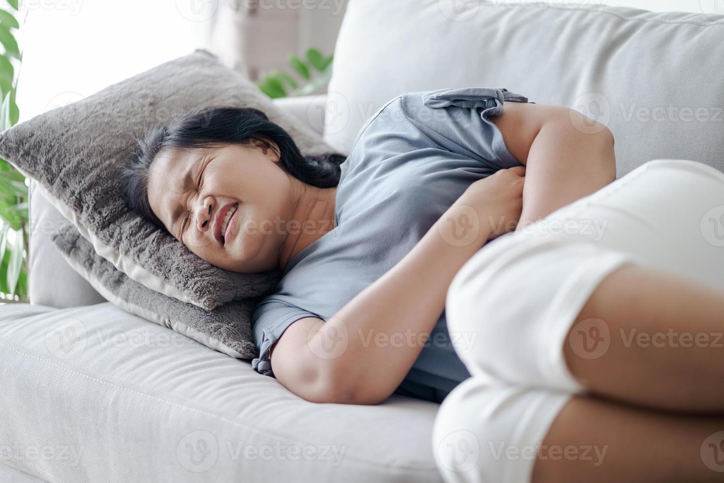 vrouw die lijdt aan buikpijn liggend op de bank thuis. buikpijn, gastritis, menstruatie, menstruatie. foto