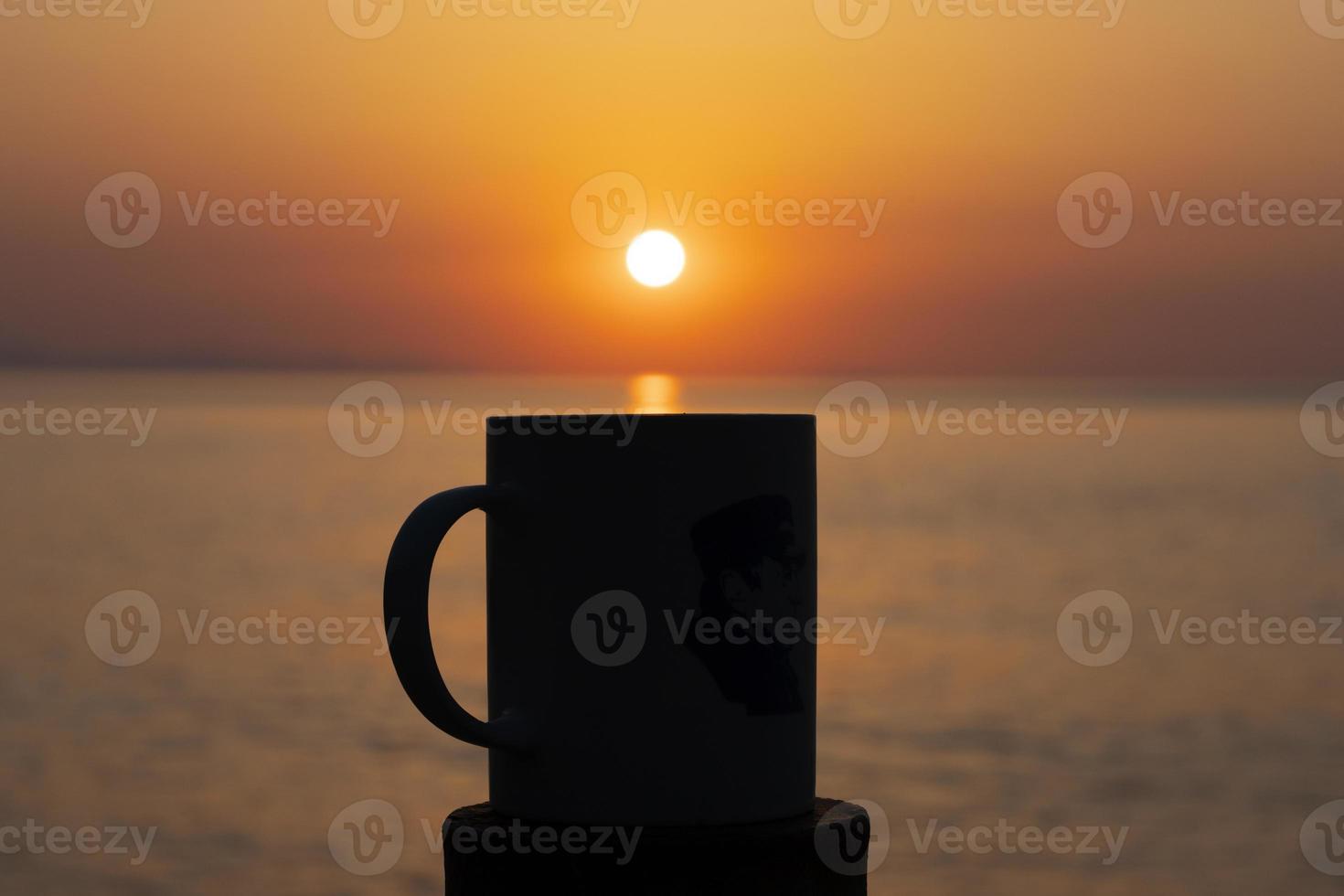 selectieve focus afbeelding van een kopje koffie of thee bij zonsopgang in de ochtend over de zee en de rijzende zon. Ik zal me concentreren op de schaduwen. foto