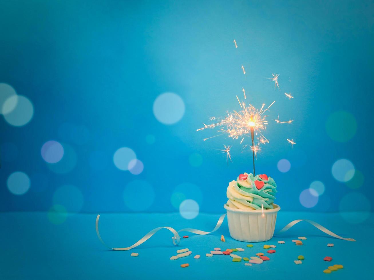 zoete cupcake en sparkler op blauwe achtergrond met kopie ruimte. gelukkig verjaardagsfeestje foto