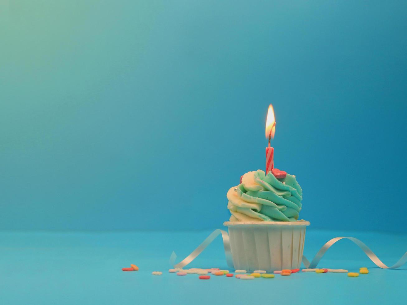 zoete cupcake en boog kaars op blauwe achtergrond met kopie ruimte. gelukkig verjaardagsfeestje foto