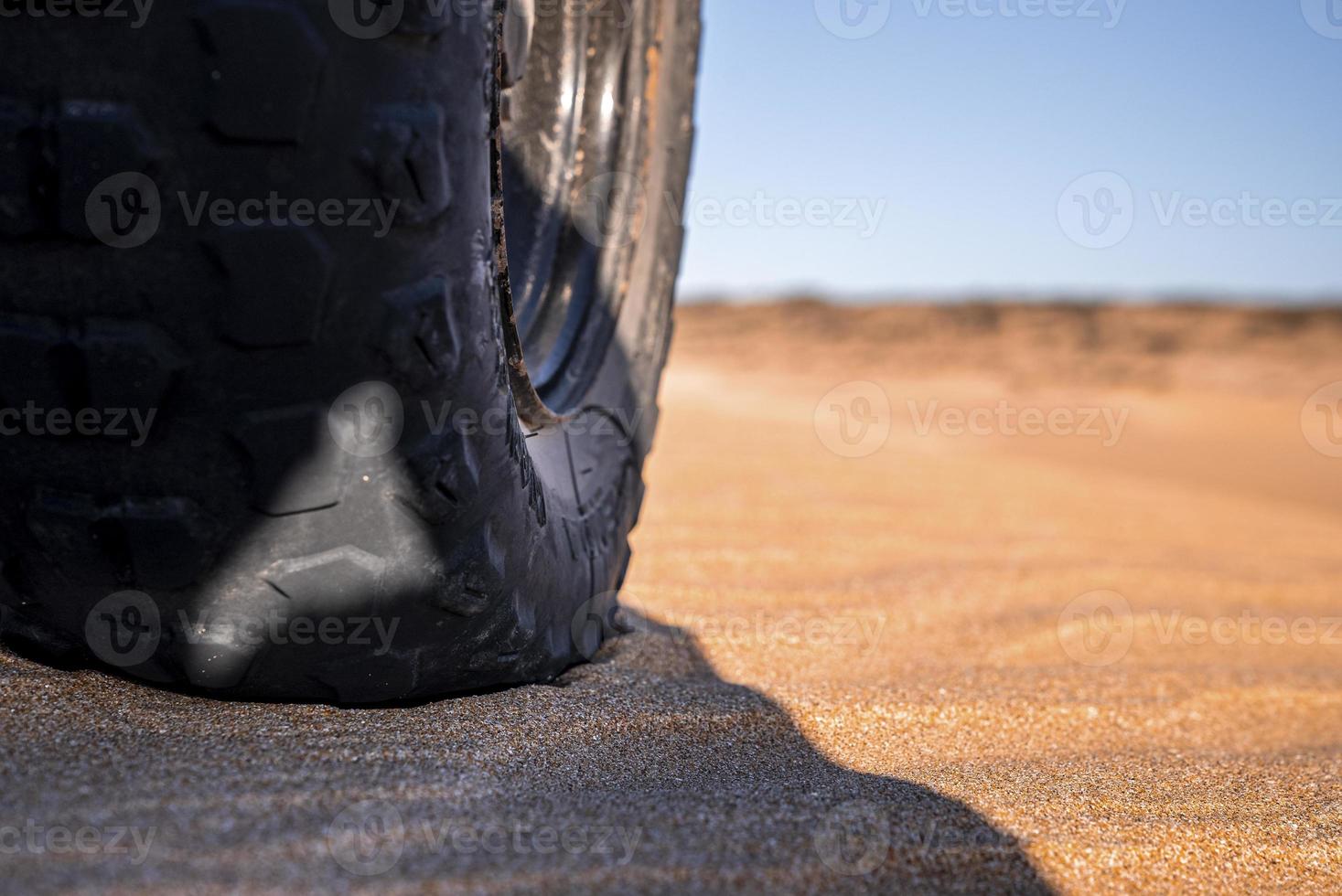 close-up van offroad-autowielen en afgeplatte band geparkeerd op zand foto