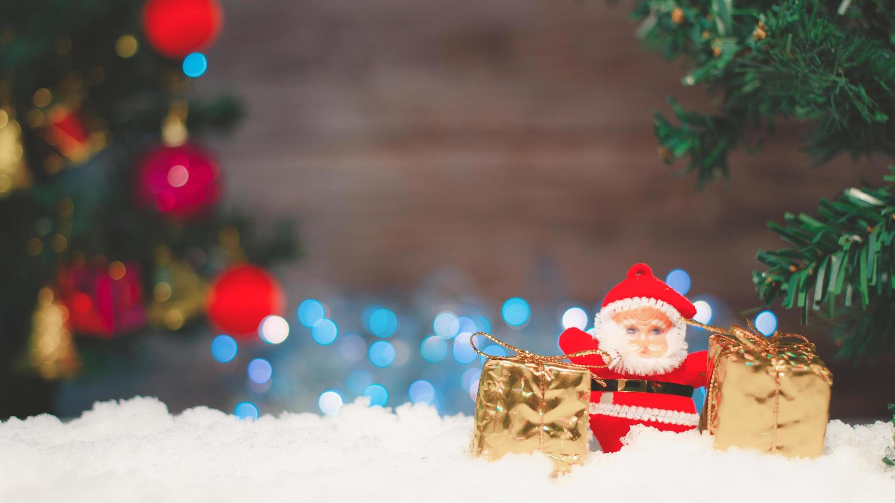 Kerstman pop met een geschenkdoos geplaatst op de sneeuw en de kerstboom achtergrond met bokeh en wood.selective focus foto