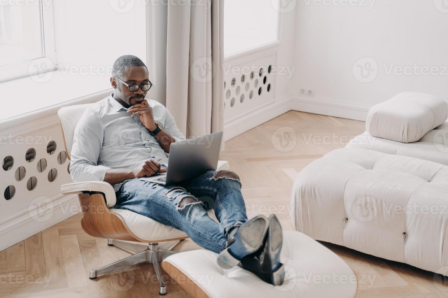zelfverzekerde professional op het werk voor de laptop. ontspannen Afrikaanse zakenman in gezellige stoel. foto