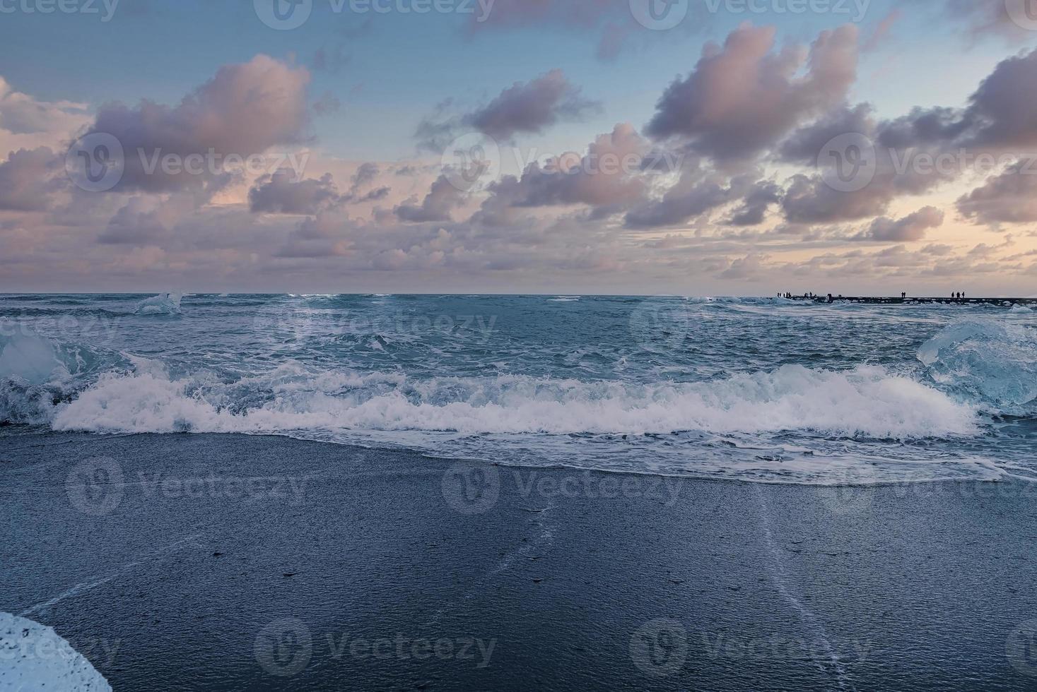 schilderachtig uitzicht op de golven op de zwarte zandkust van het diamantstrand tegen de hemel bij zonsondergang foto