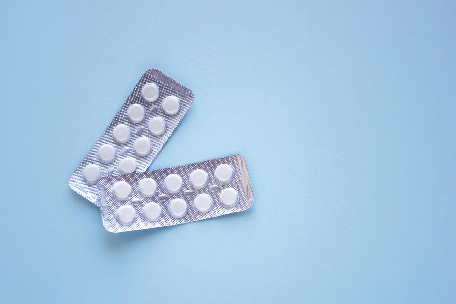twee verpakkingen van witte tabletten met kopie ruimte op blauwe achtergrond. medisch concept behandeling van ziekten, verkoop van tabletten, tabletten in blisterverpakking. foto