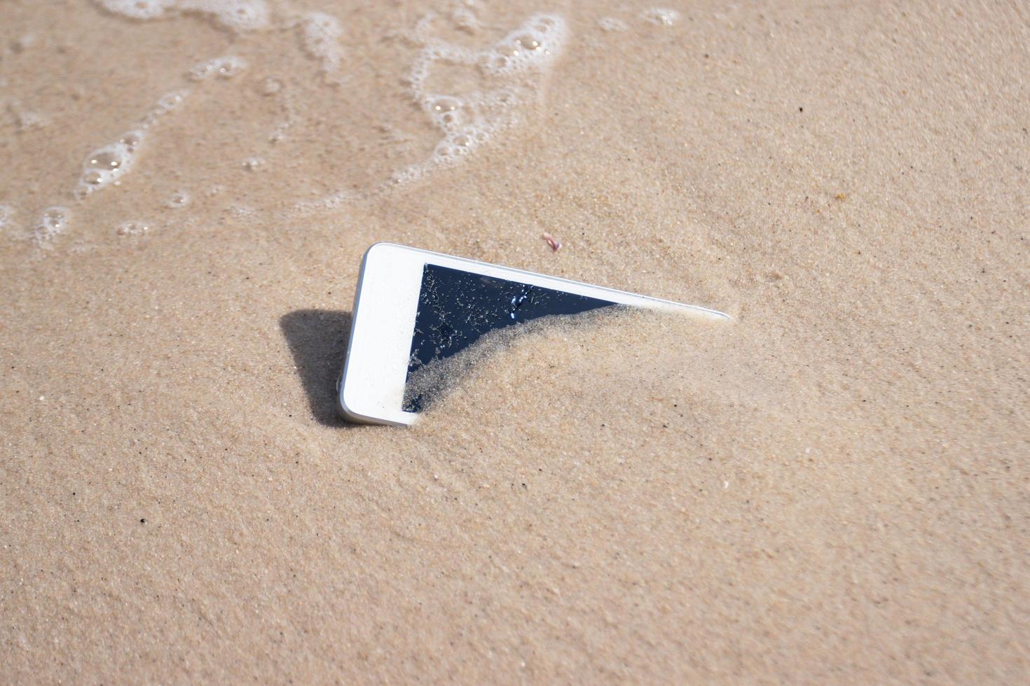 witte mobiele telefoon op zand bij strandconcept elektronisch afval foto