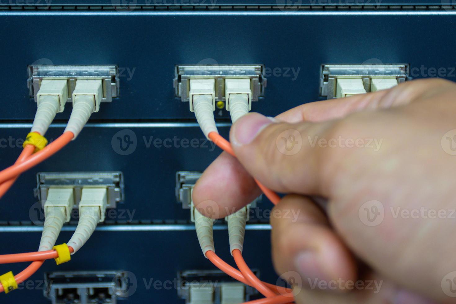 hand van een man die de glasvezelkabels van het netwerk vasthoudt om de poort van een switch aan te sluiten om het internetnetwerk aan te sluiten, conceptcommunicatietechnologie foto