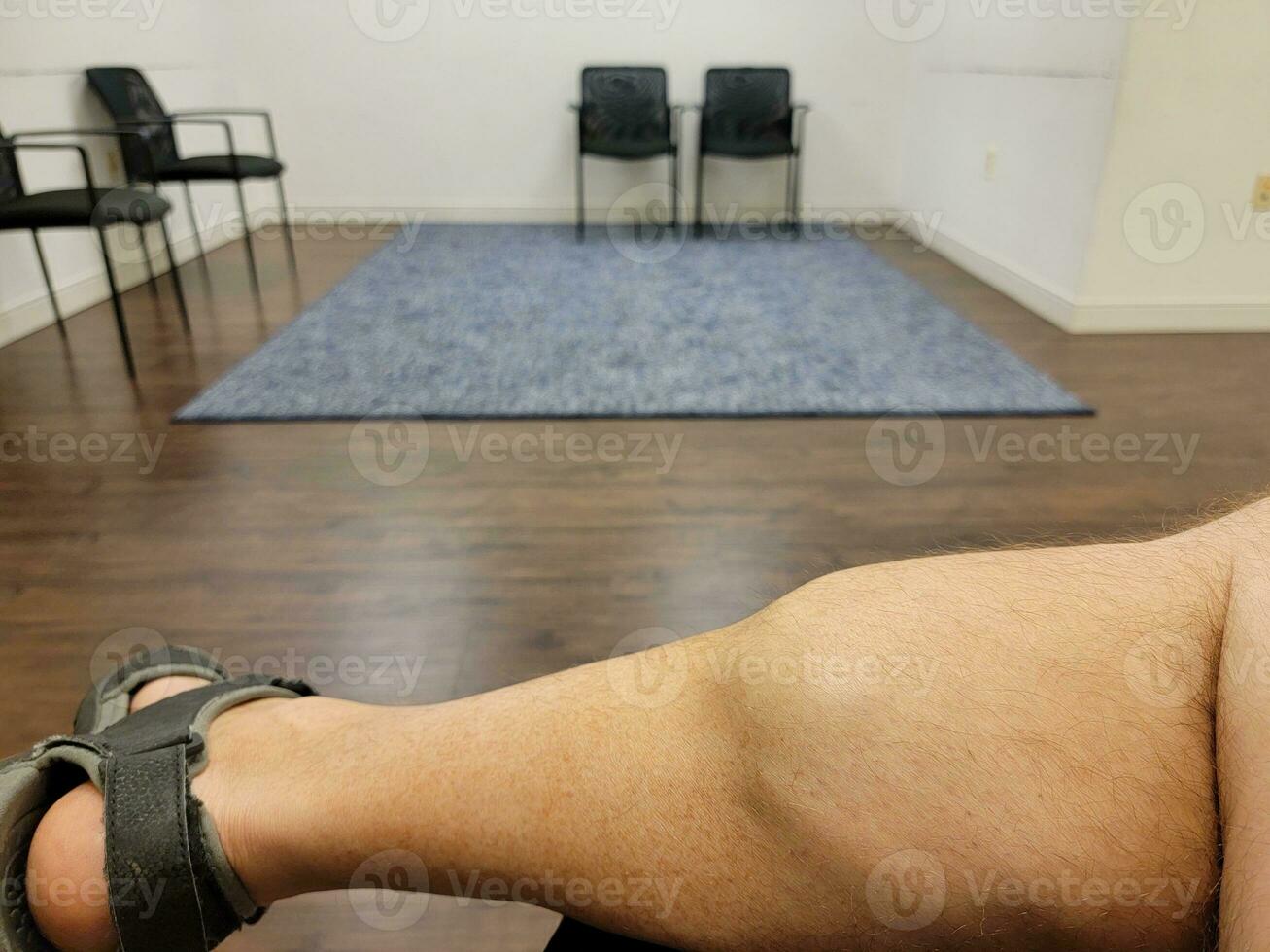 man met grote kuiten zittend in wachtkamer met stoelen foto