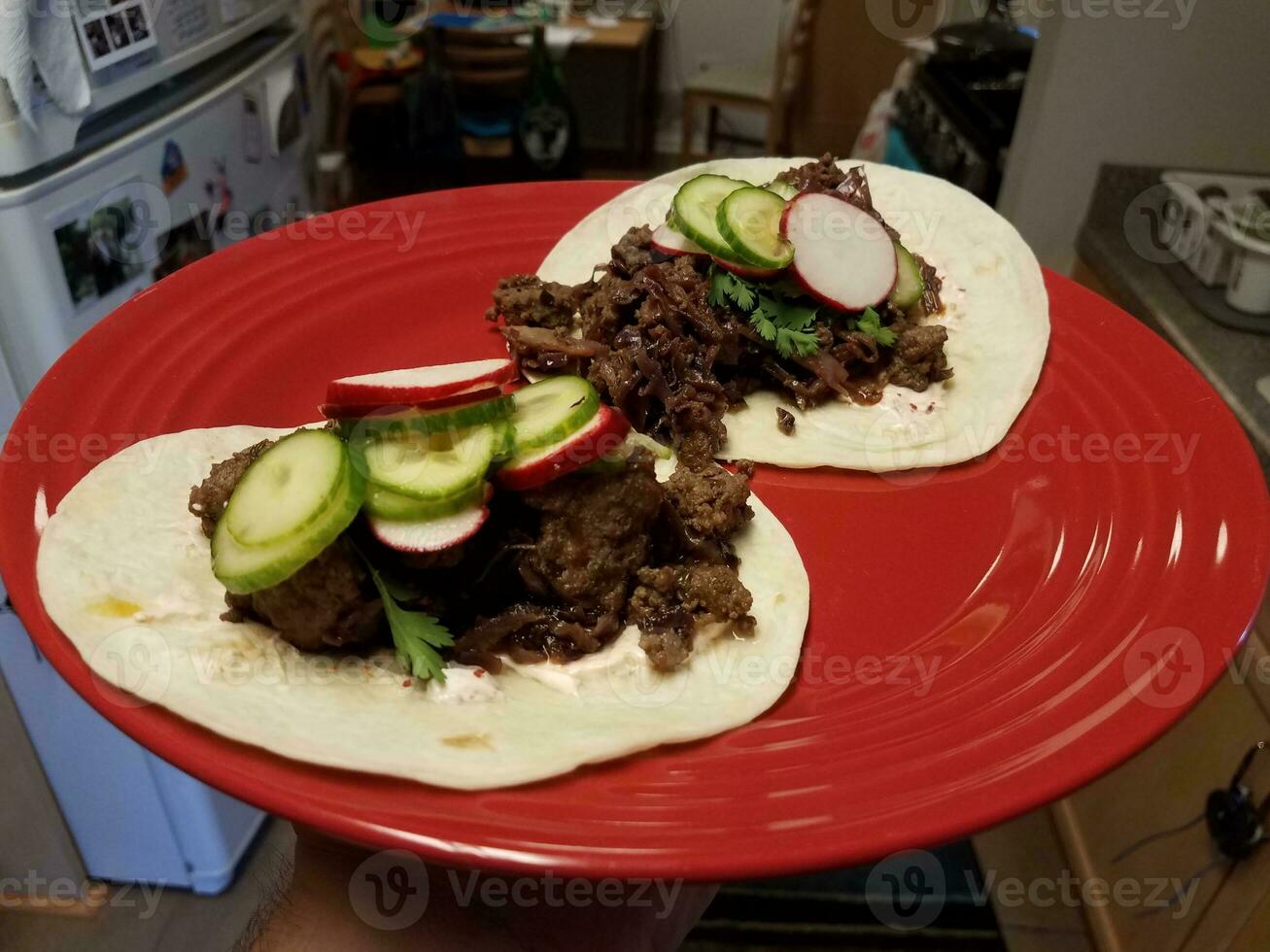 Rundvleestaco's en komkommer en radijs op rode plaat in keuken foto